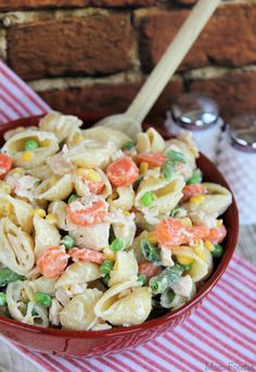 a red bowl filled with pasta salad next to a wooden spoon on top of a table