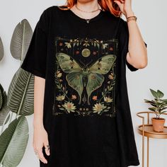 Embrace the enchanting beauty of nature with our Vintage Luna Moth T-shirt, perfect for those who adore the Cottagecore aesthetic. Made with Comfort Colors® fabric, this Luna Moth shirt exudes comfort and style. The celestial design adds a touch of mystique, ideal for the Green Witch or Dark Academia enthusiast. This Cottagecore botanical moth shirt embodies the essence of Goblincore aesthetic, making it a unique and thoughtful gift for her. Elevate your wardrobe with this mystical moon tee that Summer Fairy Grunge T-shirt With Crew Neck, Fairycore Graphic Print Short Sleeve T-shirt, Black Fairy Grunge T-shirt For Summer, Summer Fairycore Crew Neck T-shirt, Summer Fairycore Top With Graphic Print, Black Fairycore Crew Neck Top, Black Botanical Graphic Print Tops, Black Botanical Tops With Graphic Print, Moth Shirt