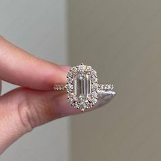 a woman's hand holding an emerald and diamond engagement ring with diamonds around it