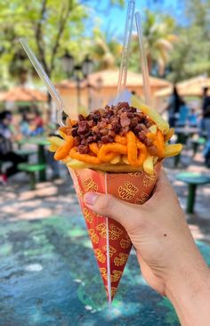 a person holding up a paper cone filled with fries and other food on top of it