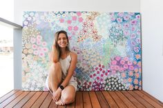 a woman is sitting on the floor in front of a painting that looks like flowers