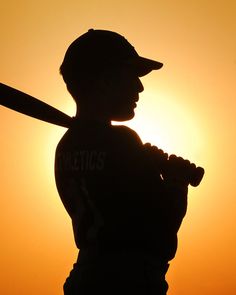 the silhouette of a baseball player holding a bat in front of an orange and yellow sky