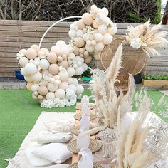 a table topped with lots of white balloons and flowers next to a wooden fence covered in grass