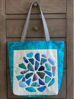 a blue and white tote bag hanging on a wooden wall with sea glass pieces in it