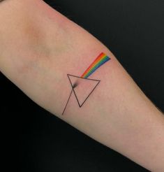 a person's arm with a small triangle and rainbow tattoo on the left forearm