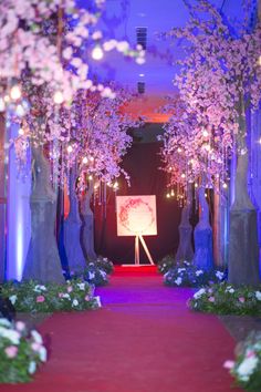 a red carpeted walkway leading to trees with white flowers on them and purple lighting