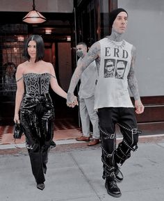 a man and woman are walking down the street holding hands while wearing black pants with chains on them