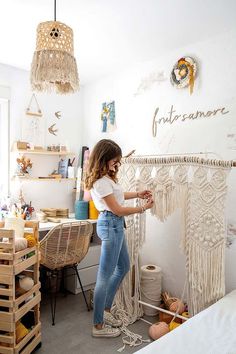 a woman standing in front of a white wall with macrame hanging from it