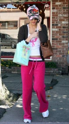 a woman in pink pants and white shirt holding up a cell phone to her face