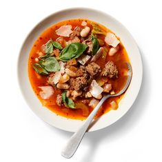 a bowl of soup with meat, beans and spinach on the side next to a spoon