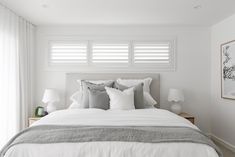 a bed with white sheets and pillows in a bedroom next to two lamps on either side of the bed