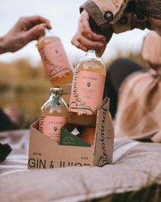 three bottles of gin and tonic sitting on top of a table next to two people