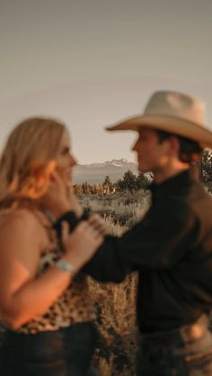 a man and woman are standing in the grass together, one is wearing a cowboy hat