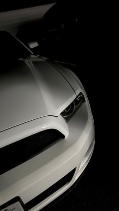 the front end of a white sports car parked in a dark spot with its lights on