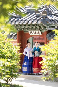 two women in traditional chinese dress standing under an archway