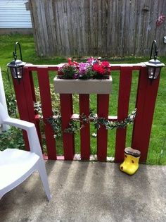 a wooden fence with flowers and rain boots on the ground next to two white chairs