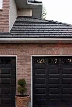 two black garage doors are open in front of a brick building with potted plants