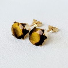 Exude elegance and confidence with these captivating genuine tiger's eye stud earrings. Each earring features a polished tiger's eye gemstone, renowned for its distinctive golden to reddish-brown bands that shimmer in the light, reminiscent of a tiger's eye. Set in a sleek and durable metal base, these earrings provide a secure and comfortable fit for everyday wear. Perfect for adding a touch of natural beauty and sophistication to any outfit, these Tiger's Eye stud earrings are a versatile addi Gold Birthstone Earrings Fine Jewelry, Fine Jewelry Gold Earrings With Birthstone, Brown 14k Gold Gemstone Jewelry, 14k Gold Brown Gemstone Jewelry, Brown 14k Gold Jewelry With Gemstones, 14k Gold Jewelry With Brown Gemstones, Gold Sterling Silver Earrings With Birthstone, Gold Birthstone Earrings, Gold Birthstone Round Earrings