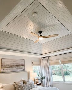 a bed room with a neatly made bed and a ceiling fan in the middle of it