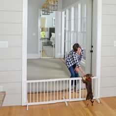 a woman standing next to a dog on top of a hard wood floor in front of a white door