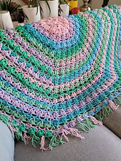 a crocheted blanket sitting on top of a couch next to a potted plant