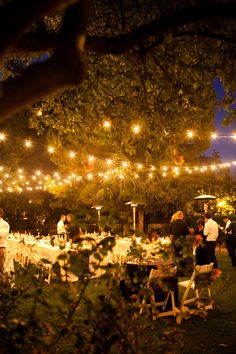 an outdoor event with tables and chairs set up for dinner under the trees at night