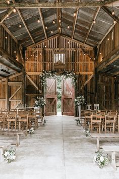 the inside of an old barn with wooden chairs and flowers on the aisle leading up to the doors