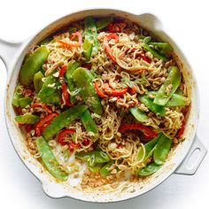 a pot filled with noodles and vegetables on top of a white countertop next to a fork