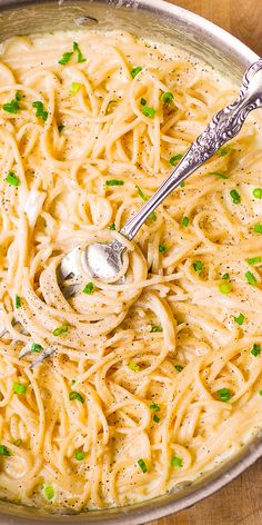 a pan filled with pasta and peas on top of a wooden table next to a silver spoon