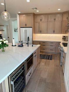 a kitchen with white counter tops and wooden flooring next to a wine cooler in the center