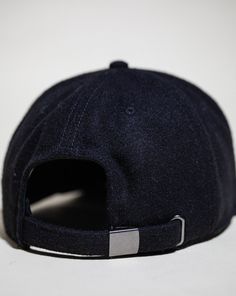 a black baseball cap with a metal buckle on the front and back side, sitting on a white surface