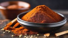 a bowl filled with red powder next to two wooden spoons and spices on a table