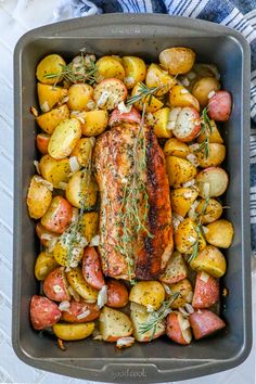 salmon and potatoes in a roasting pan with rosemary garnish on the side