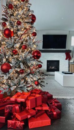 a decorated christmas tree with red and silver presents under it in front of a fireplace