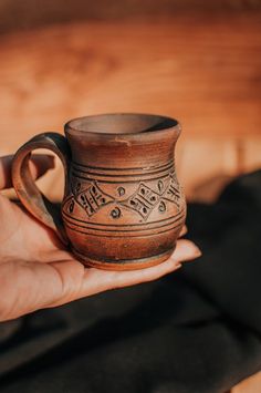 a hand holding a brown mug with designs on it's side and the handle