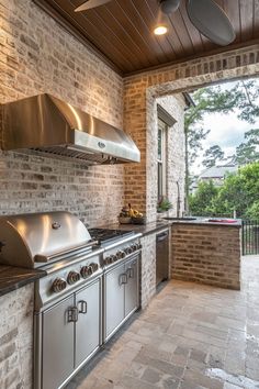 an outdoor kitchen with stainless steel appliances and brick walls, along with large windows to the backyard