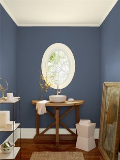 a bathroom with blue walls and a round window in the corner, along with a wooden table that has a white bowl on it