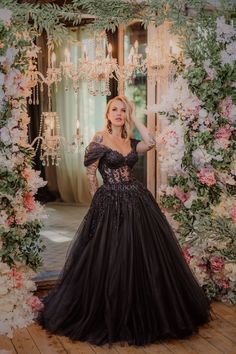 a woman in a black dress standing next to a floral arch with chandeliers