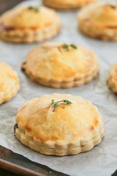 several small pies sitting on top of a baking pan covered in wax paper and garnished with green herbs