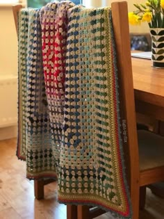 a crocheted blanket hanging from a wooden chair next to a vase with flowers