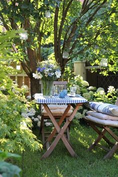 an outdoor table and chair in the grass with flowers on it, next to a tree