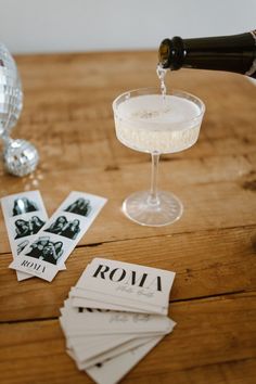 a person pouring wine into a glass on top of a wooden table next to cards