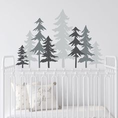 a baby's crib with trees on the wall and a white crib