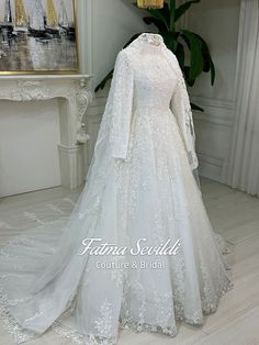 a white wedding gown with long sleeves and lace on the skirt is displayed in front of a fireplace