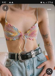 a woman with tattoos wearing a bra top and denim shorts is holding her stomach in front of the camera