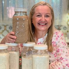 a woman is holding up some jars in front of her