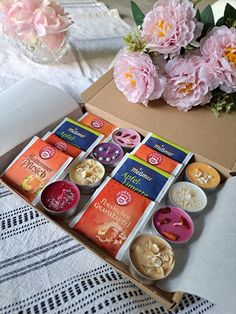 an open box filled with different types of buttons next to pink flowers on a table