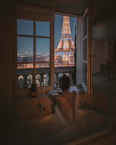 a person sitting in a bathtub with the eiffel tower lit up