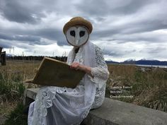 an owl mask sitting on top of a stone bench next to a book in front of a cloudy sky