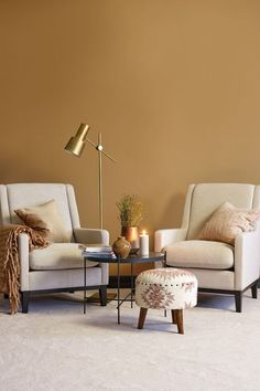 a living room with two chairs and a coffee table in front of a brown wall